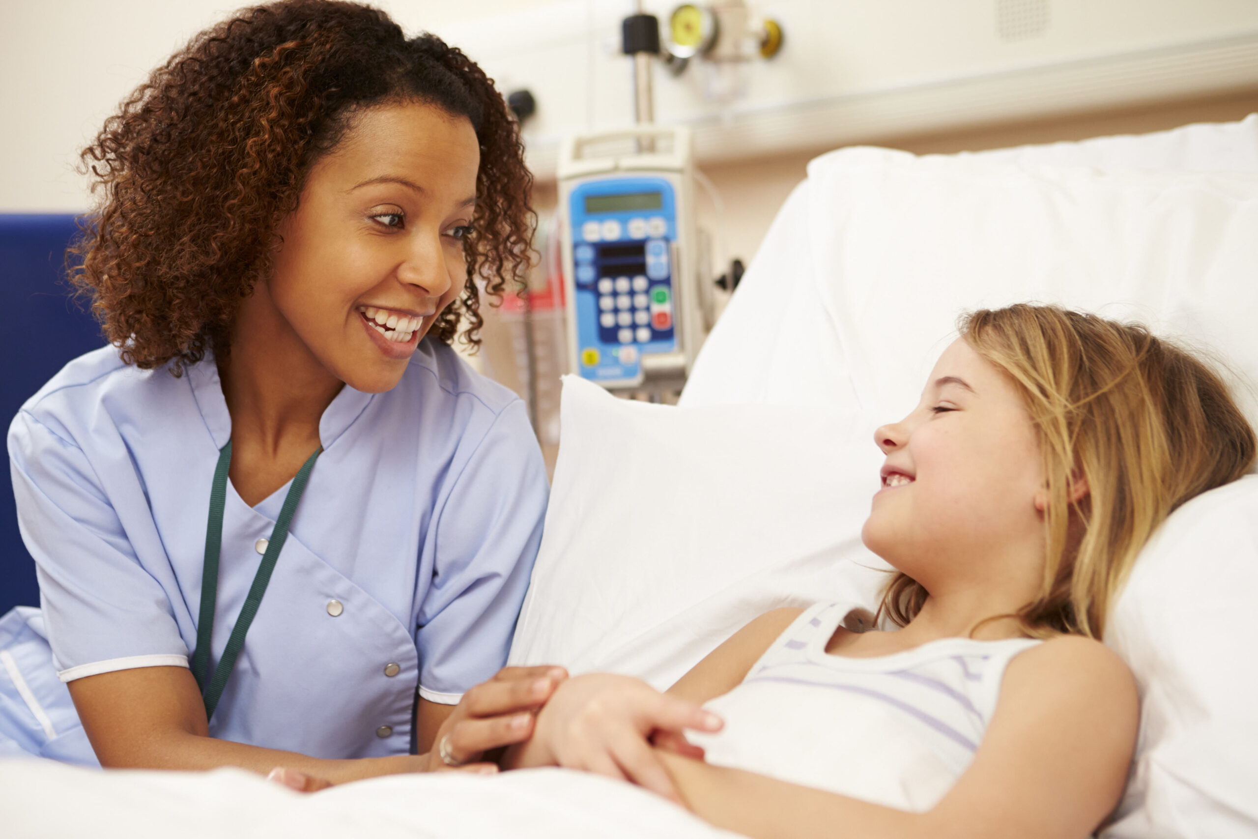A nurse sitting by a young girl's bed in the hospital.