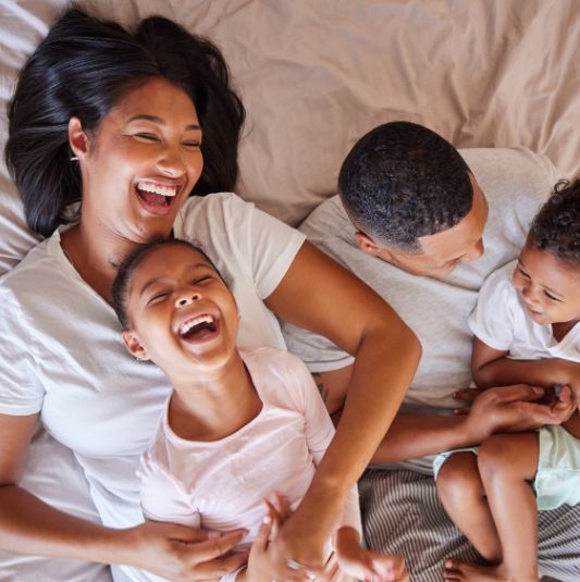 Family Laughing Together in Bed A family lying on a bed together while playing and laughing.