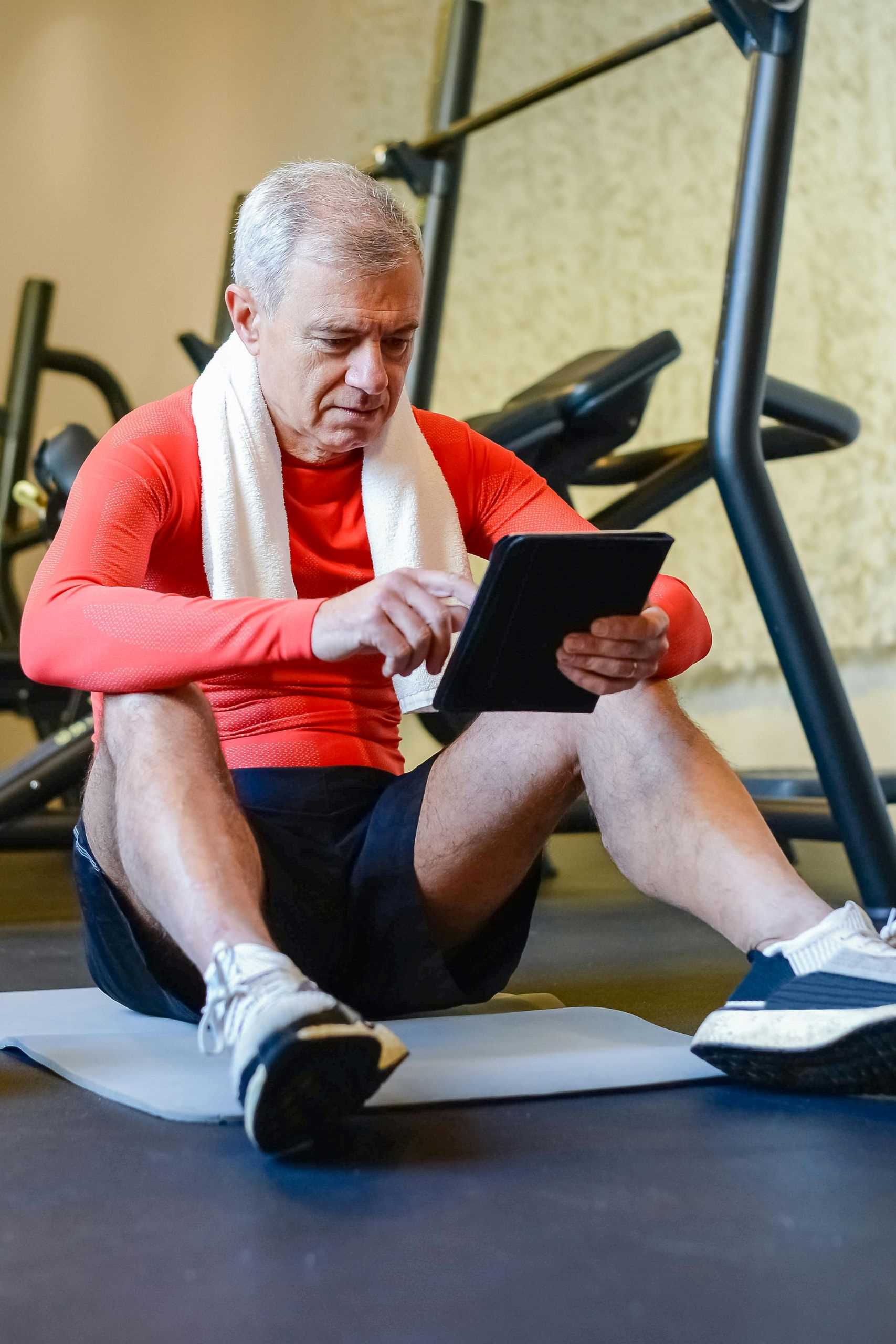 Man Sitting in Gym A man sitting in a gym while reading an iPad that is connected to his XO-SOLE PRO insoles.