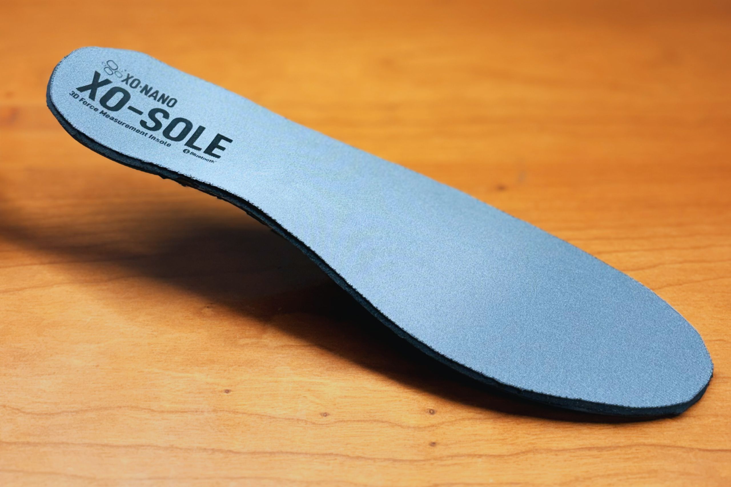 Close-up of a single XO-SOLE insole floating on a wooden table.
